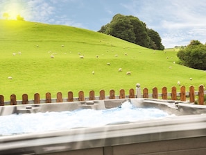 A hot tub with a wooden fence in the foreground, a grassy hill with sheep in the background, and a tree. - Hafan: A Charming Retreat in Llanerfyl (Welshpool)