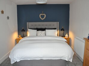 A bedroom with a large bed, two bedside tables, a nightstand, a wall-mounted heart decoration, and a radiator. - Hafan: A Charming Retreat in Llanerfyl (Welshpool)