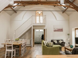 Ein geräumiges Loft mit Essbereich, einem grünen Sofa, einer Treppe und Blick ins Freie.