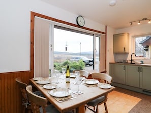 A dining area with a table set for four, a bottle of wine, and a view of the countryside.