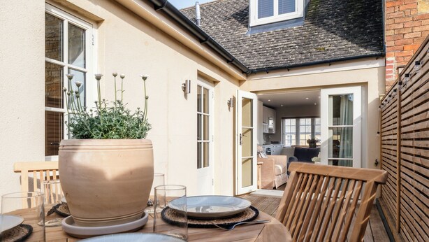 Une terrasse avec une table dressée pour le repas, une grande plante en pot et une chaise en bois.
