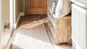 Un couloir avec une porte en bois, un banc avec des coussins, une plante suspendue et un porte-manteau.