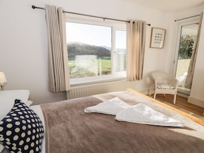 Ein Schlafzimmer mit großem Fenster, einem Bett mit brauner Decke, einem Kissen mit Punkten und einem Sessel.