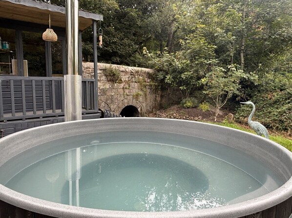 Un jacuzzi en un entorno natural con terraza de madera y pared de piedra.