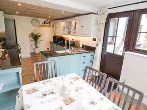 Una cocina con una mesa de comedor para dos personas, un reloj en la pared y una ventana con cortinas.