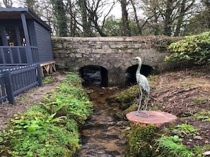 Un arroyo estrecho con un puente de piedra, una estructura de madera y una escultura de metal.