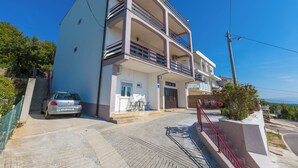 Un edificio de varios pisos con un coche estacionado frente a él, una escalera y vistas al mar.