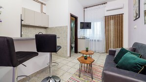Un espacio habitable compacto con kitchenette, un sofá, una mesita y un televisor.