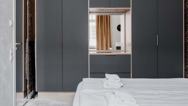 Une chambre à coucher moderne avec un grand lit, une armoire grise et un lustre original.