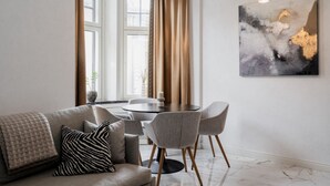Un salon moderne comprenant un canapé, une table à manger avec des chaises, un grand tableau abstrait et une fenêtre avec des rideaux.