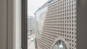 Une vue par la fenêtre sur un bâtiment à la façade quadrillée et à la structure incurvée.
