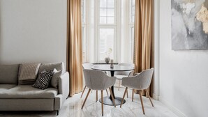 Un salon moderne avec un canapé, une table à manger ronde entourée de chaises et une grande fenêtre agrémentée de rideaux.
