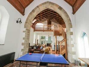 Habitació amb taula de ping-pong, un arc de pedra, una escala de fusta i vista cap a una zona de menjador.
