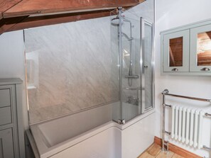 Et badeværelse med brusekabine i glas, en hvid radiator og et træloft.