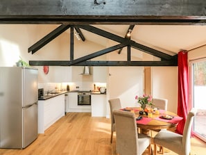 Eine moderne Küche mit Holzbalken, einem Essbereich mit gedecktem Tisch für zwei Personen und Blick ins Freie.