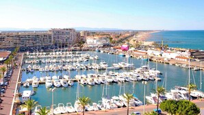 A marina with numerous boats docked, a beach in the background, and a cityscape with buildings. - Air-conditioned house for 6 with supervised swimming pool - Beach & port on foot - Terrace (Saint-Cyprien)