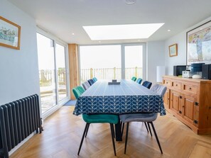 A modern dining room with a large table, chairs, a radiator, and a view of the outdoors. - Charming Pink House with Views (St. Austell)