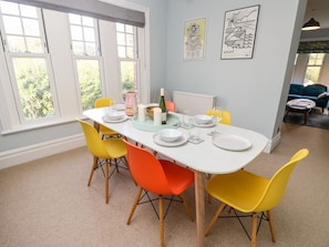 A dining area with a white table, yellow and orange chairs, and a view of greenery outside. - 5 The Nab House, Bembridge (Bembridge)