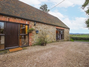 A stone building with a gravel driveway, wooden doors, and a small garden area.