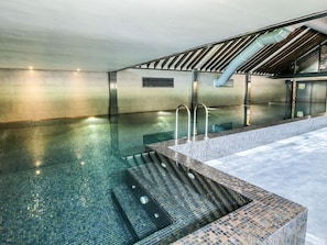 Una piscina con escalones de acceso, un área de terraza con baldosas y una sección cubierta con techo inclinado.