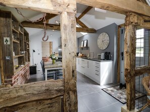 Une cuisine rustique avec des poutres apparentes, une table à manger en bois et un îlot central doté d’une horloge.