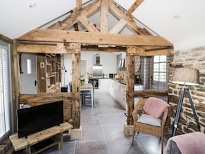 Un intérieur rustique avec des poutres apparentes, un téléviseur posé sur un meuble en bois, une chaise en osier et une lampe.