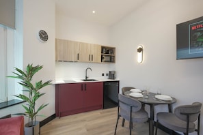A compact kitchen with a sink, microwave, and cabinets, a dining table with chairs, and a clock on the wall. - The Sixty | Luxury 2BR Apt with Secure Parking (Cardiff)
