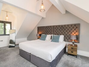 Ein Schlafzimmer mit einem großen Bett, einem Kopfteil, Nachttischlampen, einem Nachttisch und einem Fenster.