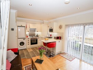 A compact kitchen with modern appliances, a dining area with red chairs, and a large sliding glass door to a balcony. - Church View, Ambleside (Ambleside)