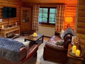 A cozy cabin interior with a wooden interior, a television mounted on the wall, a fireplace, and a window with curtains. - Little Bears Hideaway @ 23 Lakeside, Felton (Morpeth)