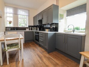 A kitchen with grey cabinets, a white countertop, a sink, and a window with a view. - Glebe Cottage, Skipton (Skipton)