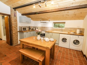 Une cuisine avec une table en bois, un banc, un lave-linge, un four à micro-ondes et une fenêtre.
