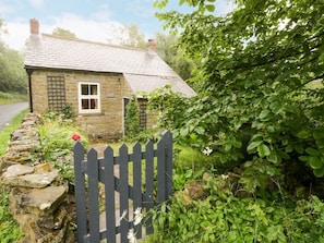 Une petite maison en pierre avec une fenêtre, un portail en bois et un mur de pierres.