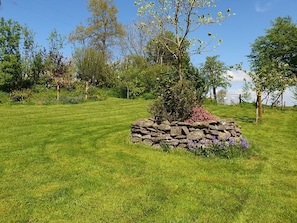 A well-maintained grassy area with a stone-built flower bed and a tree.