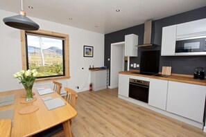 Una cocina moderna con armarios blancos, encimera de madera y un ventanal con vistas al campo.