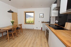 Una cocina moderna con encimera de madera, un comedor con mesa y sillas, una ventana con vistas, y una pared blanca con un cuadro enmarcado.