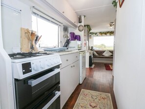 A compact kitchen with a stove, microwave, and various utensils. - Woodland Caravan, Y Ffor (Pwllheli)