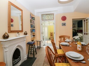 A dining area with a fireplace, a bookshelf, and a dining table set for four. - 27 Exeter Street in Teignmouth (Teignmouth)