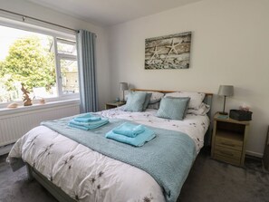 Ein Schlafzimmer mit einem Bett, zwei Nachttischen, einem Fenster mit Vorhängen, einem Wandbild und einer Heizung.