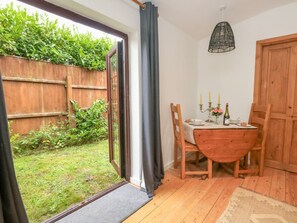 A room with a wooden table and chairs, a door, a window with curtains, and a view of a garden. - Coldharbour Farm Bungalow Annexe, Wareham (Wareham)