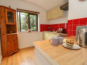 A kitchen with wooden cabinets, a window, a red-tiled backsplash, and a countertop with a plate and mug. - Coldharbour Farm Bungalow Annexe, Wareham (Wareham)
