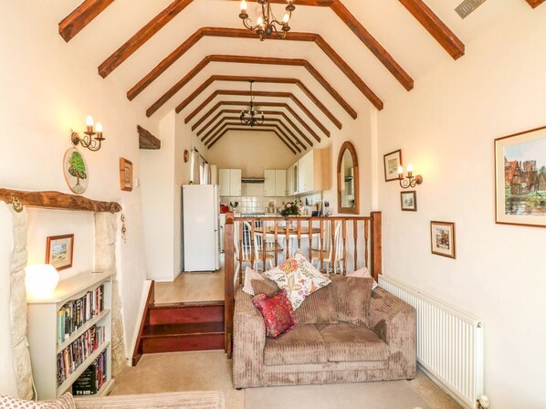 A cozy living room with a fireplace, a bookshelf, and a staircase leading to a kitchen.