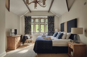 A bedroom with a large bed, a television, a wooden dresser, a chair, a window with curtains, and a chandelier. - Oughtershaw Hall, Hawes (Skipton)