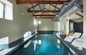 A swimming pool with a wooden ceiling structure, a shower area, and a lounge chair. - Oughtershaw Hall, Hawes (Skipton)