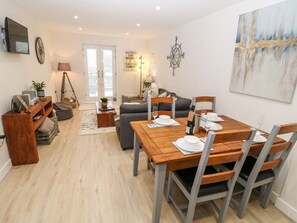 Ein modernes Wohnzimmer mit Esstisch für vier Personen, einer Couch, einem Fernseher und einer Lampe.