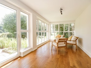 A room with large windows, wooden flooring, a wooden chair, and a ceiling light fixture.