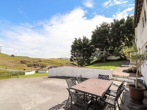 An outdoor patio with a table and chairs, surrounded by a white wall and trees. - Pyllau Farm, Llandudno (Llandudno)
