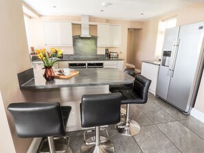 A modern kitchen with a central island, black bar stools, stainless steel appliances, and a vase with flowers. - Pyllau Farm, Llandudno (Llandudno)