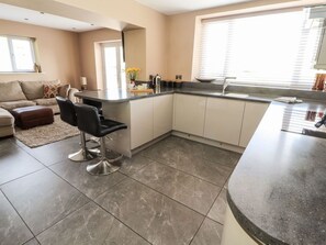 A modern kitchen with a central island, a dining area with a sofa, and a large window providing natural light. - Pyllau Farm, Llandudno (Llandudno)