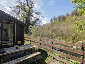 A wooden picnic table with a bottle and glass, a wooden fence, and a building with a glass door.